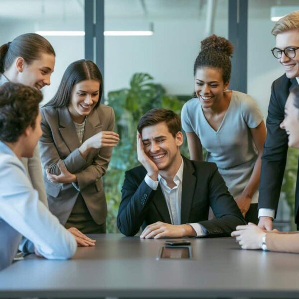 Grupo de profissionais em uma sala de reunião, com uma pessoa parecendo desapontada enquanto os outros sorriem de forma simpática.