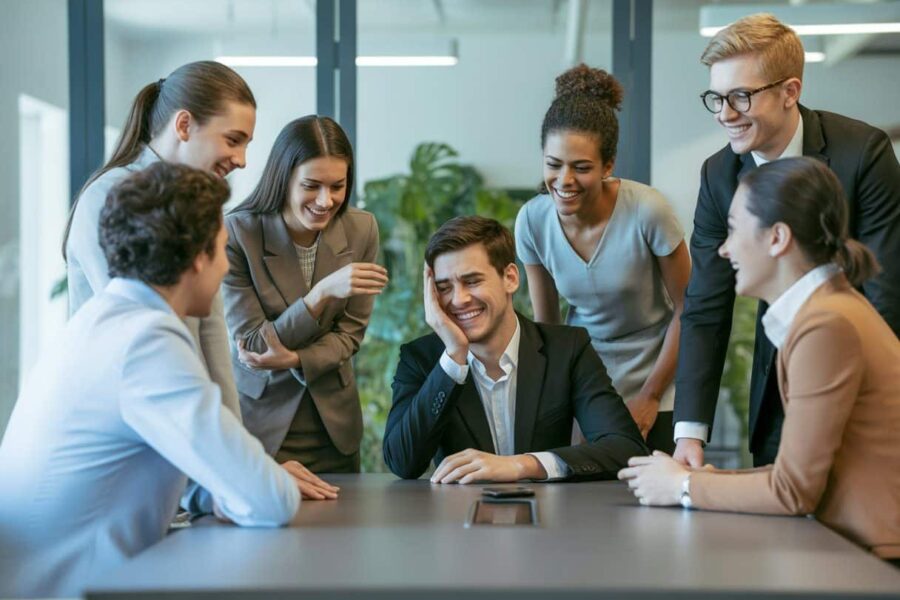 Grupo de profissionais em uma sala de reunião, com uma pessoa parecendo desapontada enquanto os outros sorriem de forma simpática.