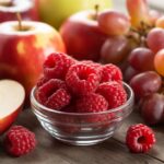 Uma tigela de framboesas vermelhas, maçãs vermelhas e cachos de uvas vermelhas sobre uma mesa de madeira.